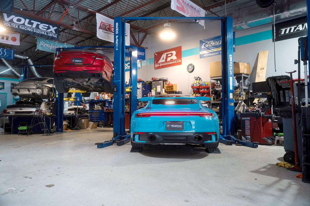 Blue Porsche 911 992 between the lifts on the Velocity Factor shop floor in Coral Springs