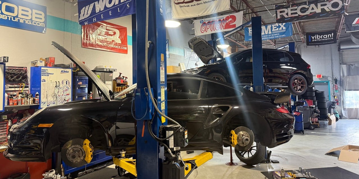 Black Porsche 911 Turbo on a lift with yellow brake calipers in the Velocity Factor shop