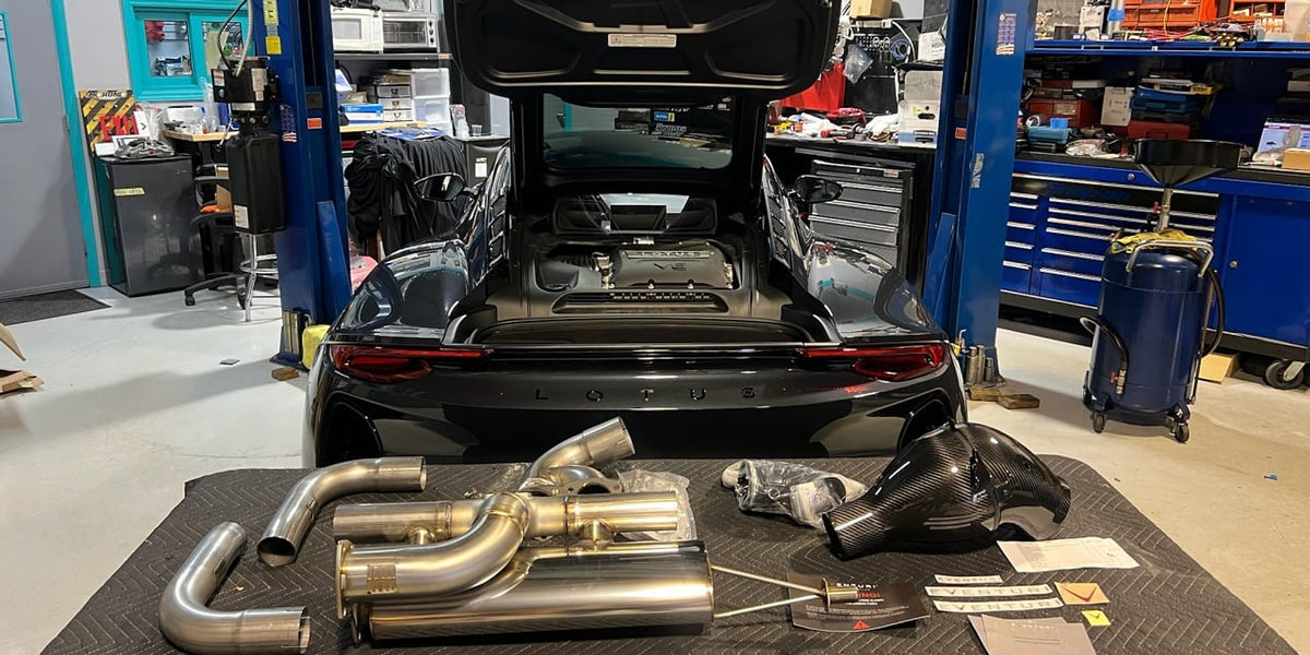 Lotus Emira in the Velocity Factor shop with an Eventuri carbon intake and a stainless exhaust laid out on the floor mat