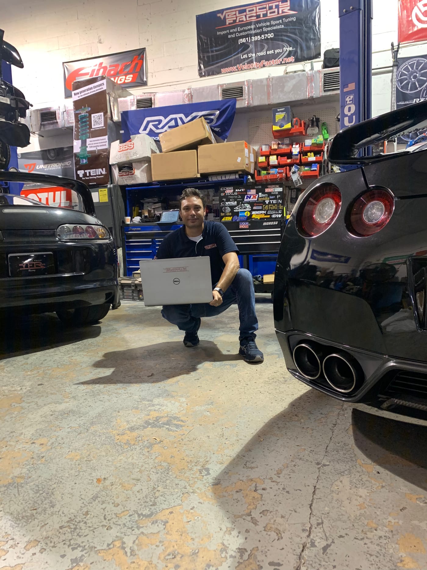 Velocity Factor team member running diagnostics on a laptop between two performance cars on the shop floor
