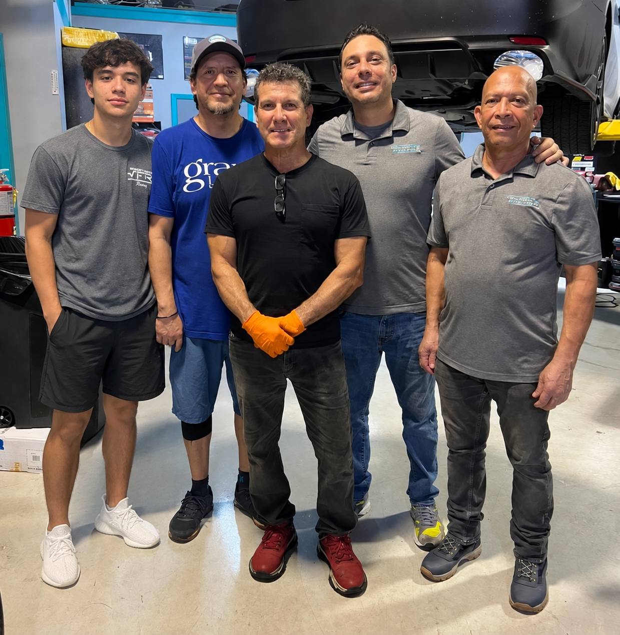 Five members of the Velocity Factor team standing together on the shop floor under a car on a lift