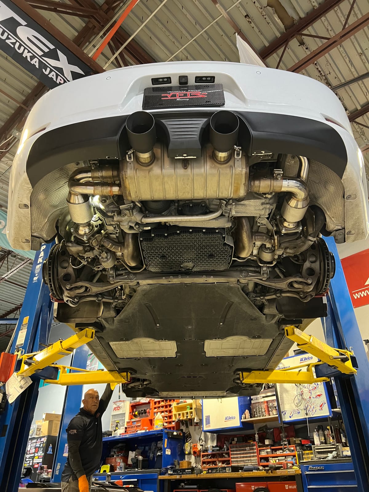 Velocity Factor technician beneath a Porsche on a lift with the exhaust system exposed