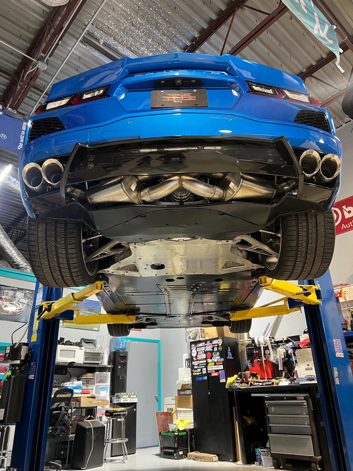 Underside of a blue Corvette C8 on the lift at Velocity Factor showing the quad-tip exhaust and rear diffuser
