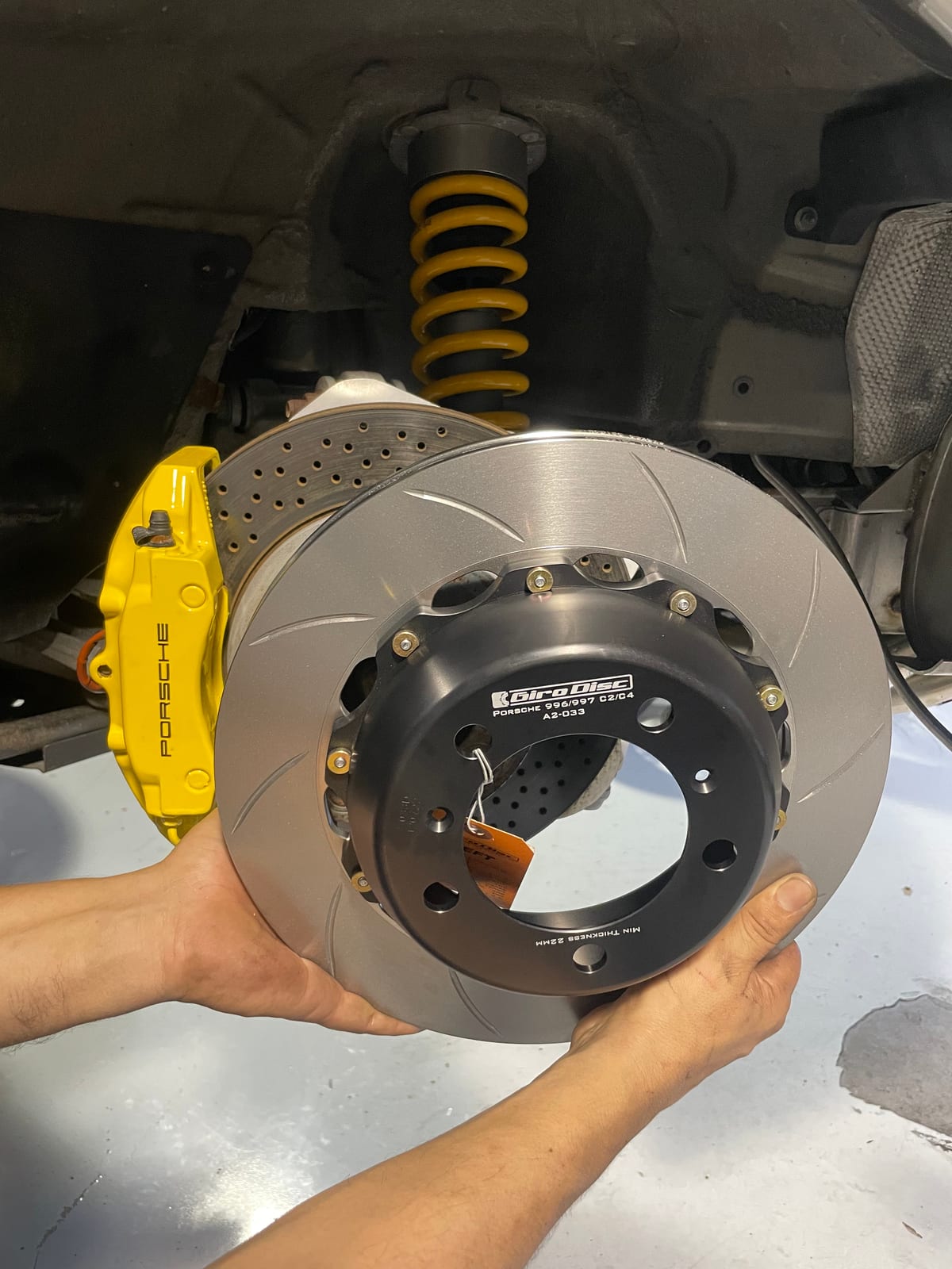 Refinished yellow Porsche brake caliper with a new Giro Disc rotor being fitted at Velocity Factor