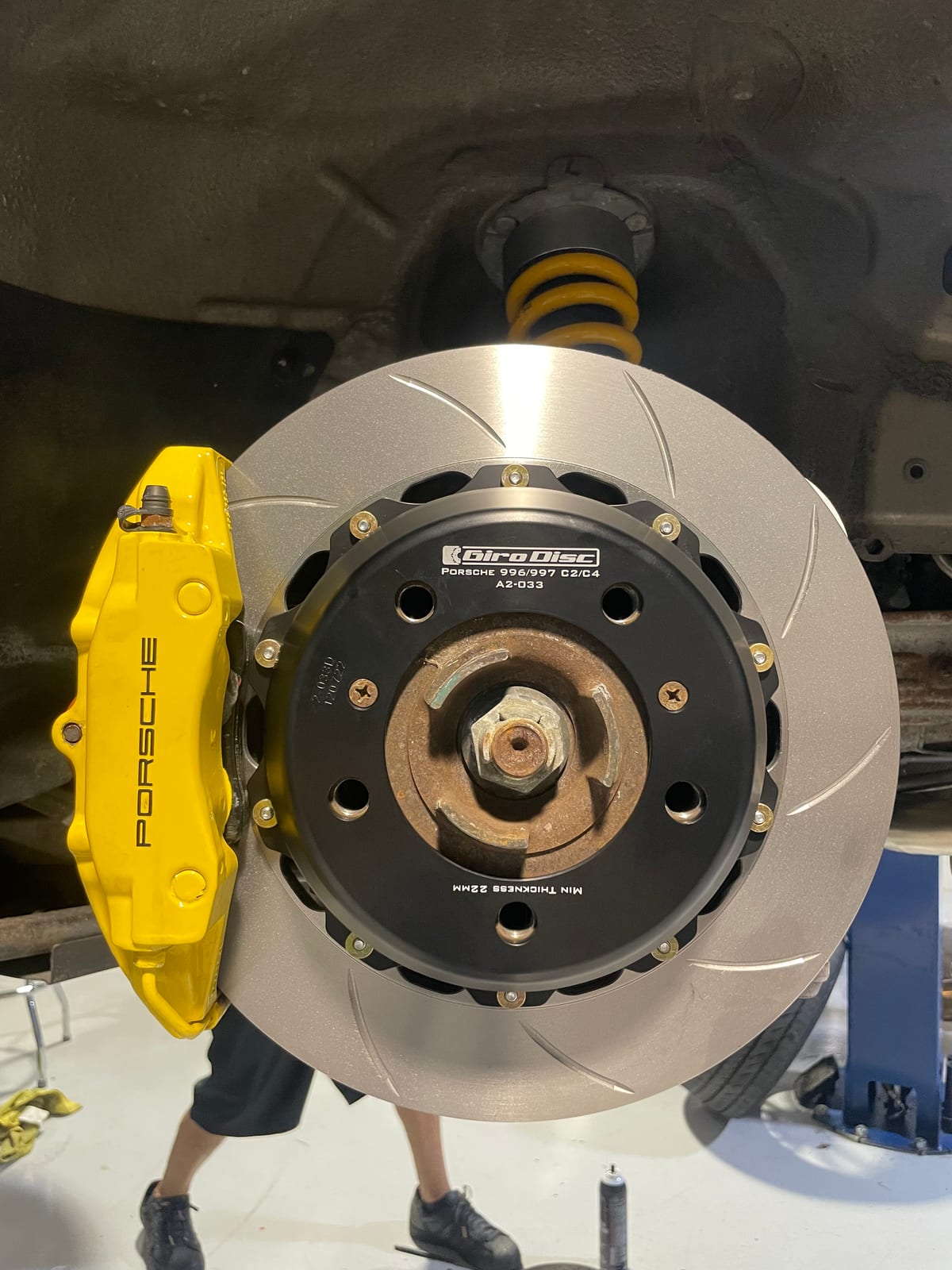 Yellow refinished Porsche brake caliper during rotor installation at Velocity Factor