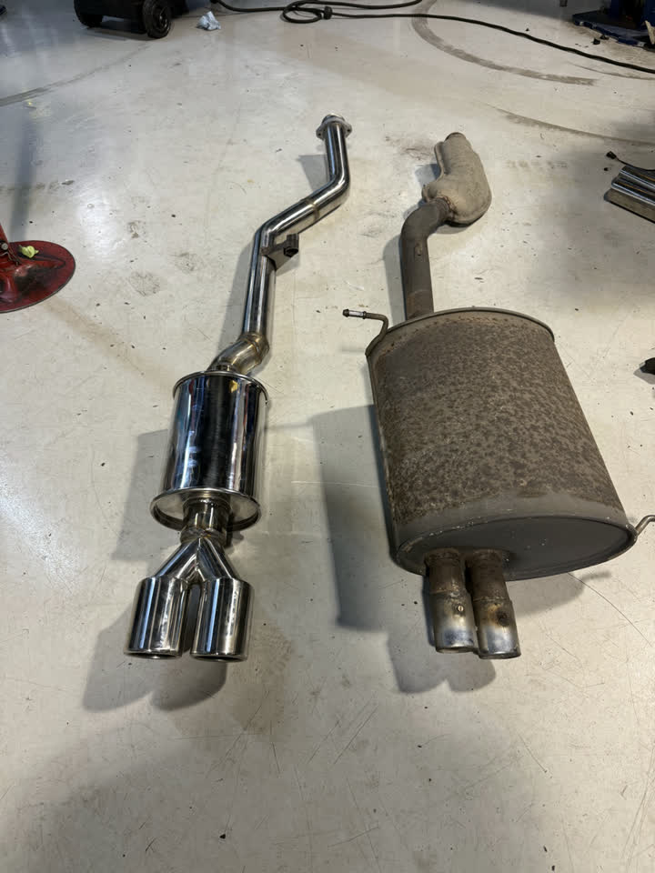 Handmade polished stainless muffler and dual tips next to the rusted factory muffler from a BMW Z3