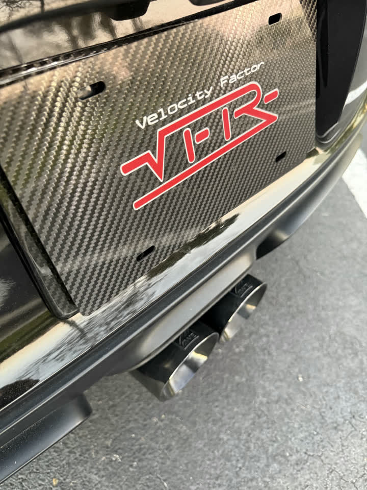 Quad exhaust tips under a black Porsche wearing a Velocity Factor carbon plate