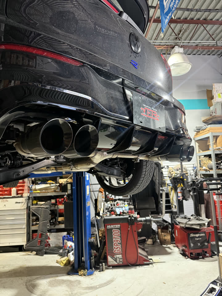 Quad exhaust tips under a black Volkswagen Golf R on the lift at Velocity Factor