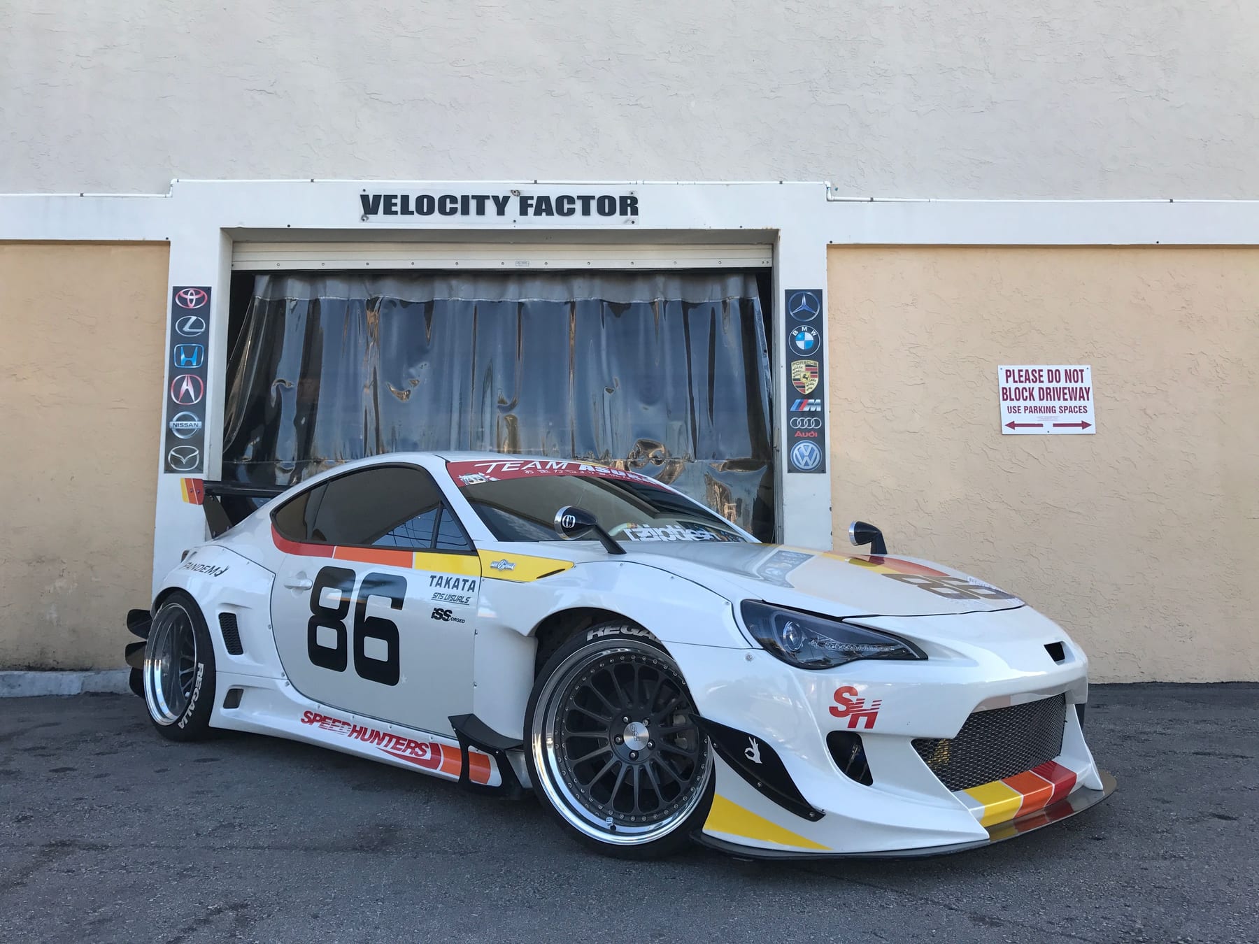 Widebody white Toyota 86 race car with number 86 livery parked in front of the Velocity Factor shop door